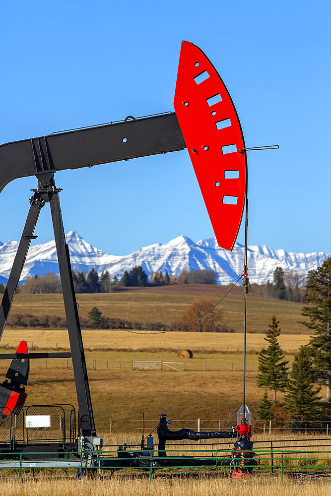 Pumpjack in a field with the foothills and snow-covered Rocky mountains in the background; Alberta, Canada