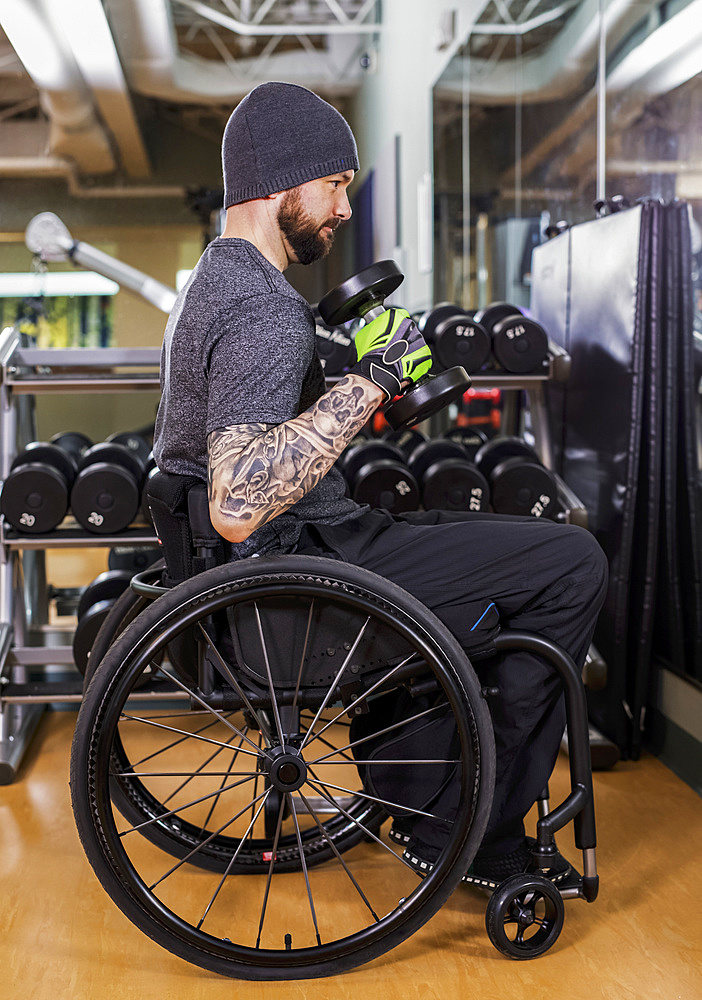 A paraplegic man working out using free weights in front of a mirror at recreational centre: Sherwood Park, Alberta, Canada