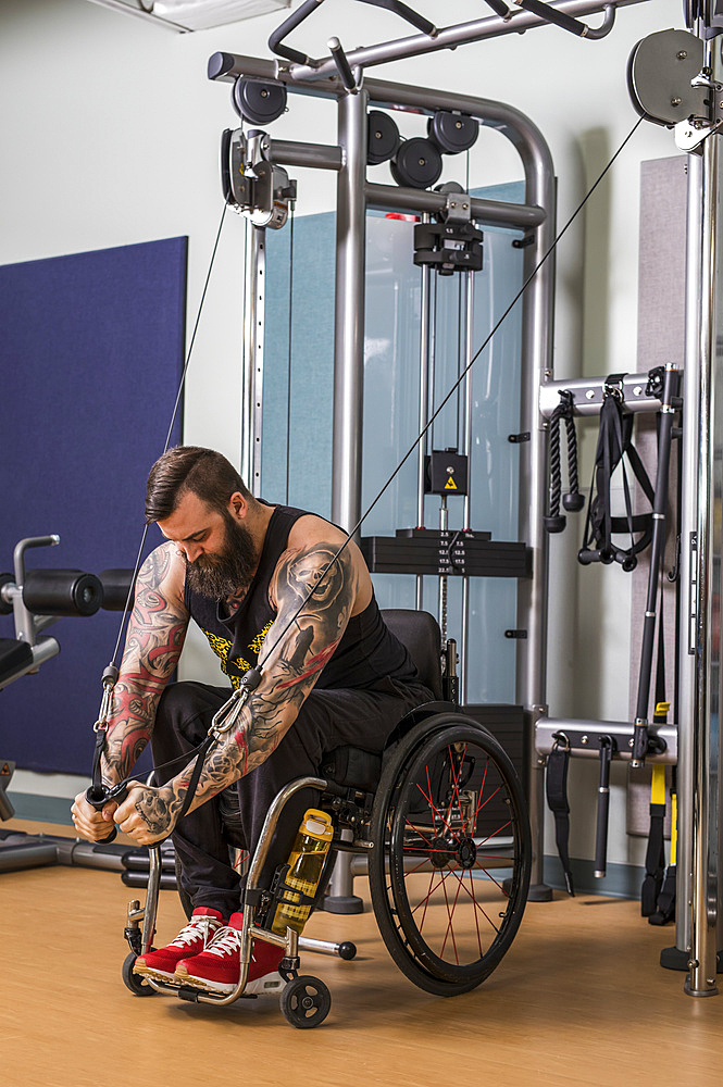 A paraplegic man working out using a crossover pulley weight lifting apparatus in a fitness facility; Sherwood Park, Alberta, Canada