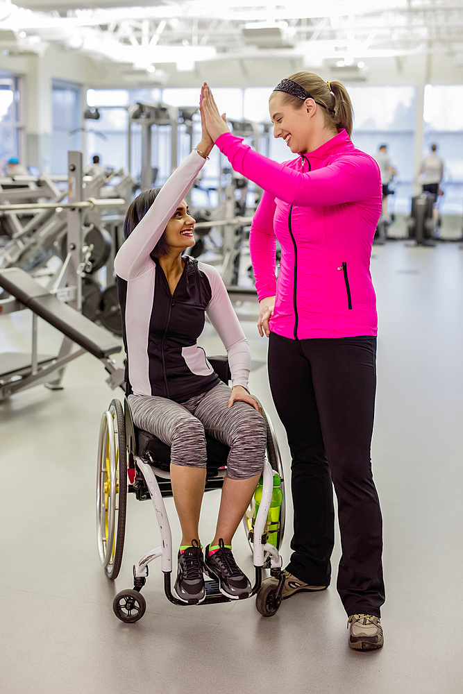 A paraplegic woman and her trainer give a high five after a successful workout in a recreational facility: Sherwood Park, Alberta, Canada