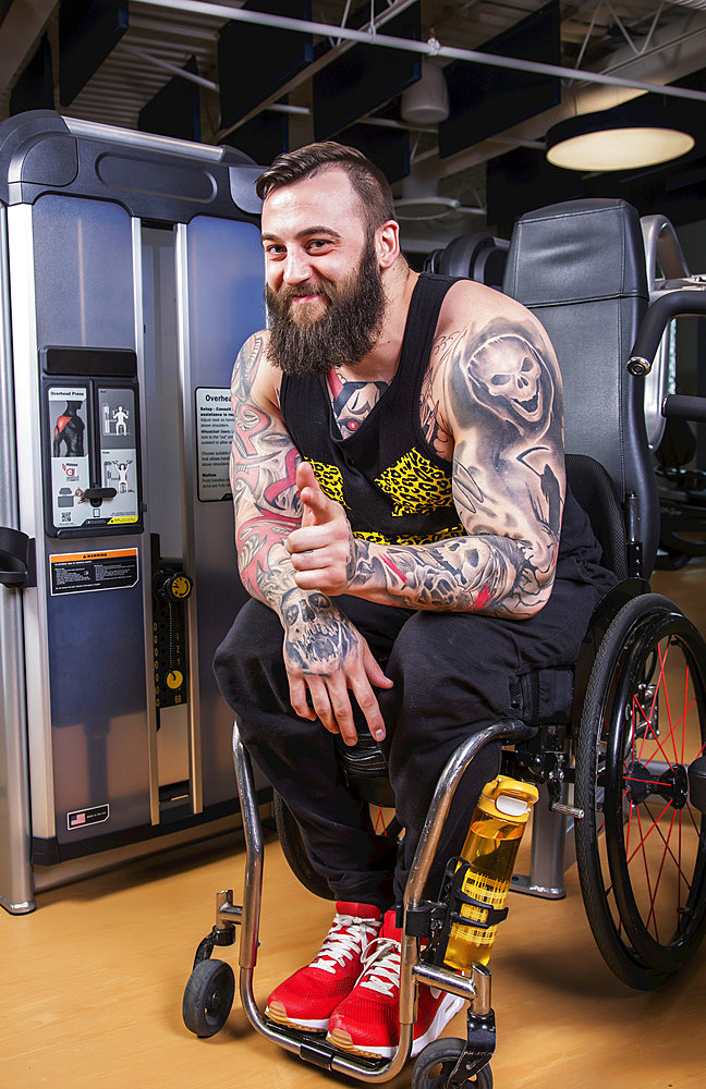 A paraplegic man looking at the camera and giving an affirming hand gesture after working out using an overhead press in a fitness facility; Sherwood Park, Alberta, Canada