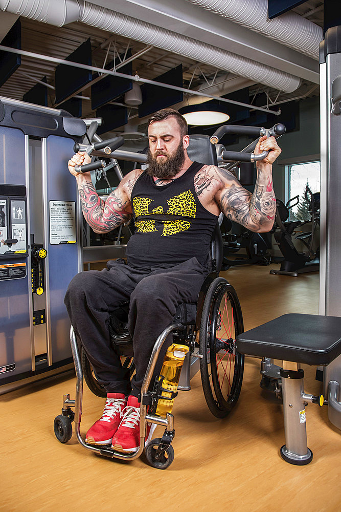 A paraplegic man working out using an overhead press in fitness facility; Sherwood Park, Alberta, Canada