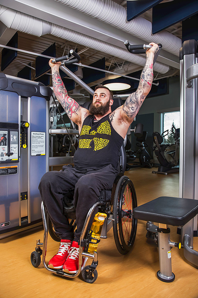 A paraplegic man working out using an overhead press in fitness facility; Sherwood Park, Alberta, Canada