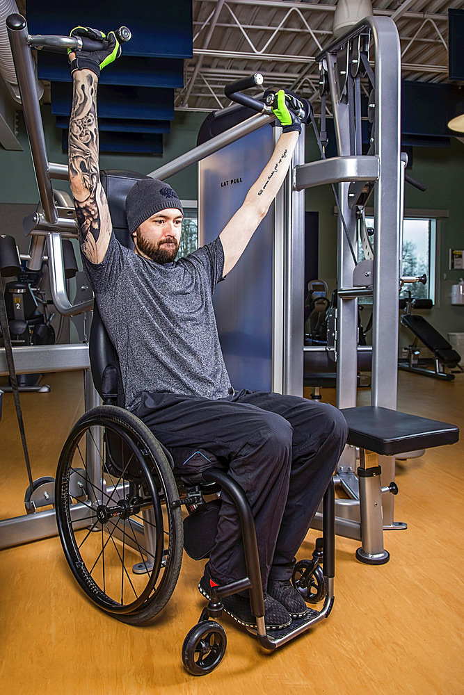 A paraplegic man working out using an overhead press in fitness facility; Sherwood Park, Alberta, Canada