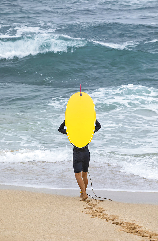 A male surfer walks on the beach towards the water with a bright yellow surfboard; Kihei, Maui, Hawaii, United States of America