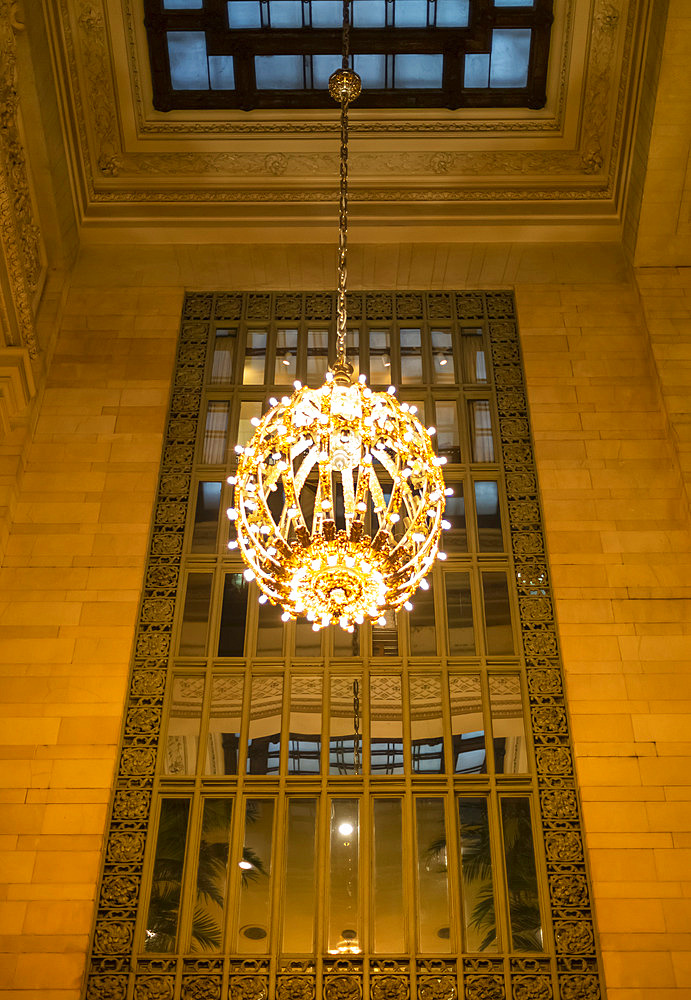 Illuminated and decorative round chandelier hanging in front of a mirror in a Manhattan building; New York City, New York, United States of America