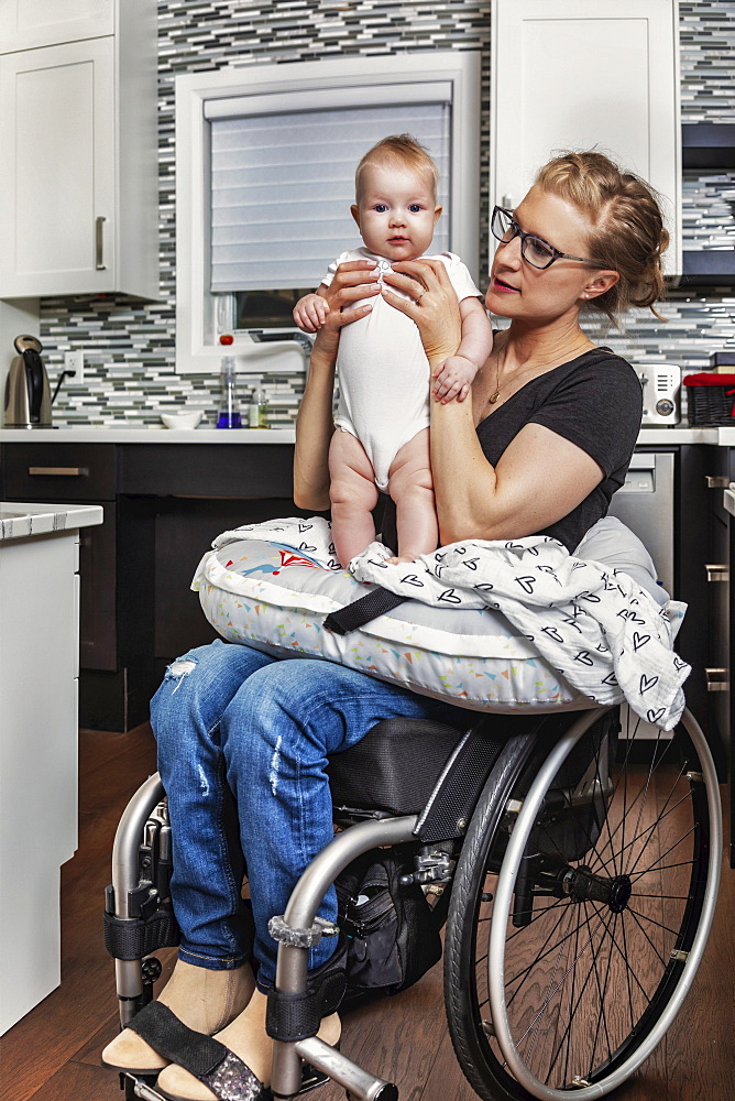 A paraplegic mother holding her baby on her lap, in her kitchen, while sitting in her wheel chair: Edmonton, Alberta, Canada