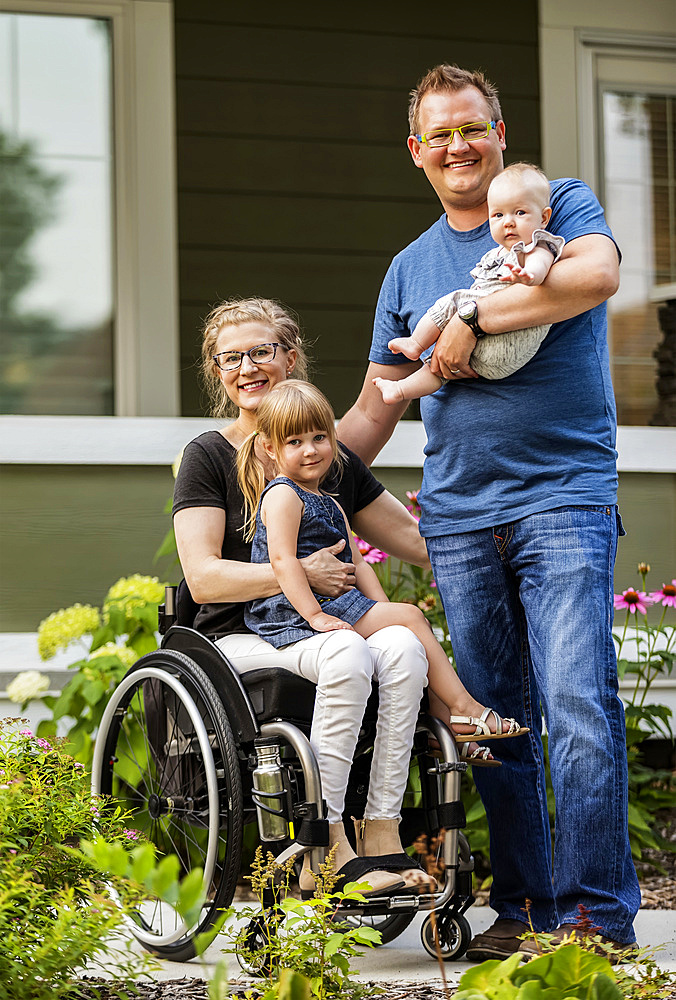 A young family posing for a family portrait outdoors in their front yard and the mother is a paraplegic in a wheelchair; Edmonton, Alberta, Canada