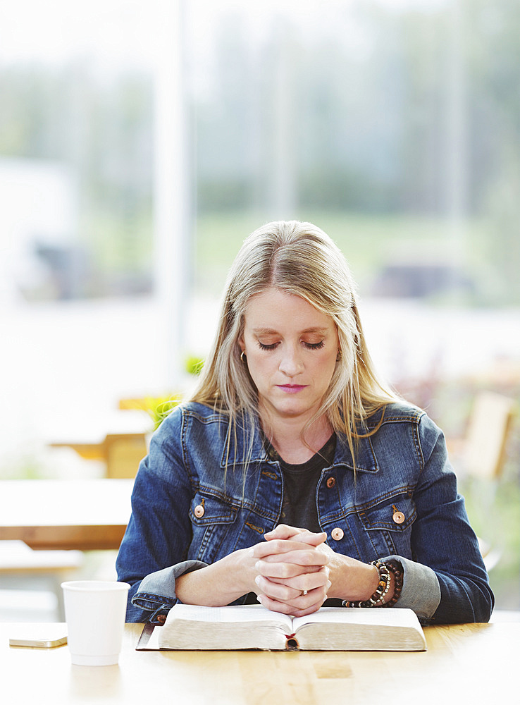 A mature woman praying, after doing some personal Bible study, in a coffee shop : Edmonton, Alberta, Canada