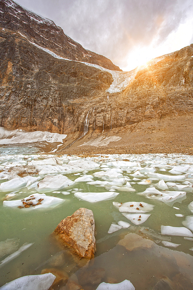 Ice chunks float in the glacial water of the Rocky Mountains with a sunburst shining bright over Mount Edith Cavell in Jasper National Park; Alberta, Canada