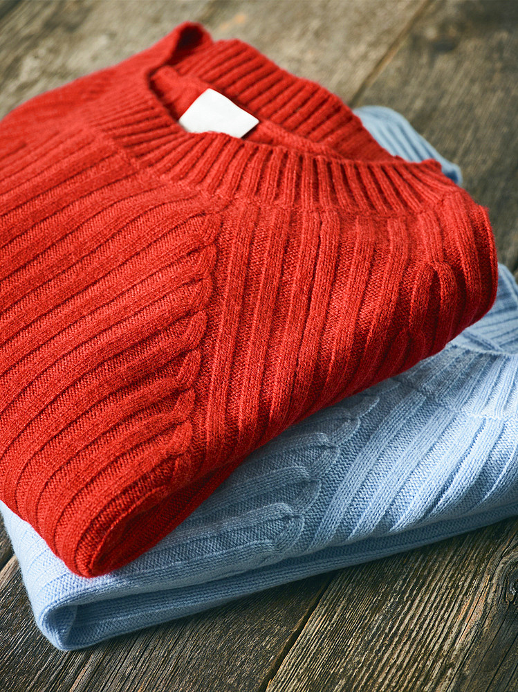 Red and blue folded sweaters on display on a wooden table; Studio