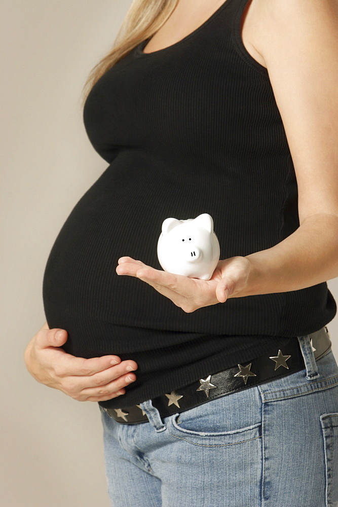 Side View Of A Pregnant Woman Holding Piggy Bank