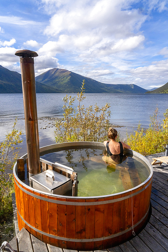 Woman sitting in a wood fired hot tub on the shore of a Yukon Lake, Yukon, Canada