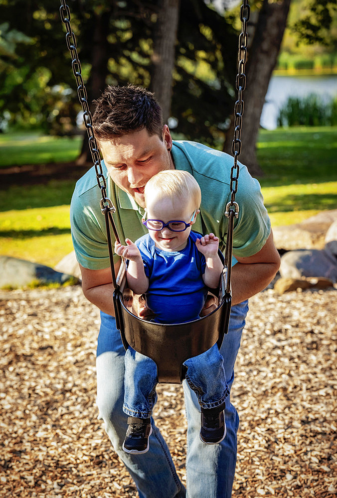 Father spending quality time with his son who has Down Syndrome, pushing him on a swing in a city park, during a warm fall afternoon, Leduc, Alberta, Canada