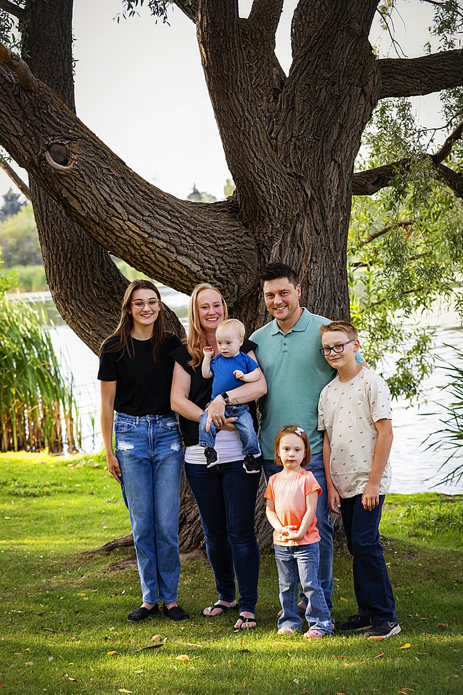 Outdoor family portrait in a city park by a lake on a warm fall afternoon and the youngest son has Down syndrome, Leduc, Alberta, Canada