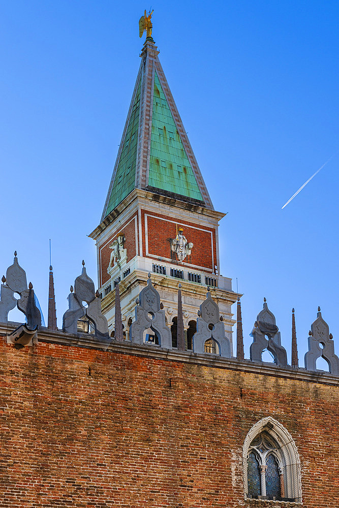 Close-up view of the pyramidal spire of St Mark's Campanile behind the decorative rooftop edging of Doge's Palace in the Piazza San Marco in Venice against a blue sky, Venice, Veneto, Italy