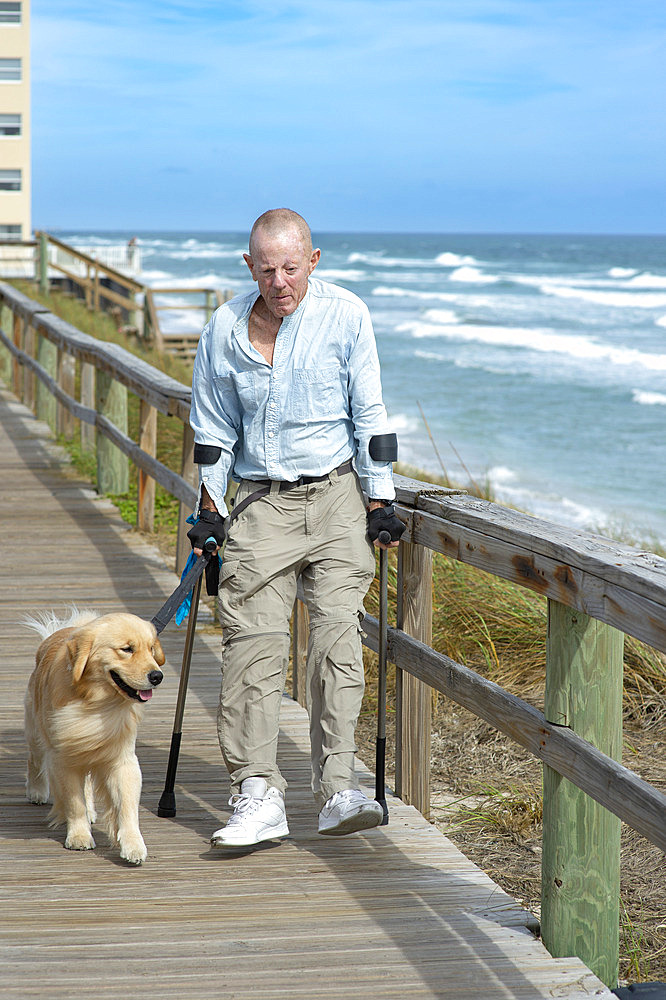 Paraplegic man with forearm crutches and service dog enjoys walking along the ocean promenade, Boynton Beach, Florida, United States of America