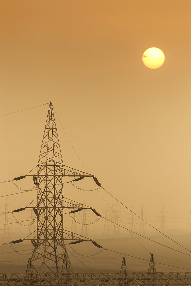 Power pylons stretch into the distance, sun rises through air thick with sand, Suez Canal, Port Said, Egypt, North Africa