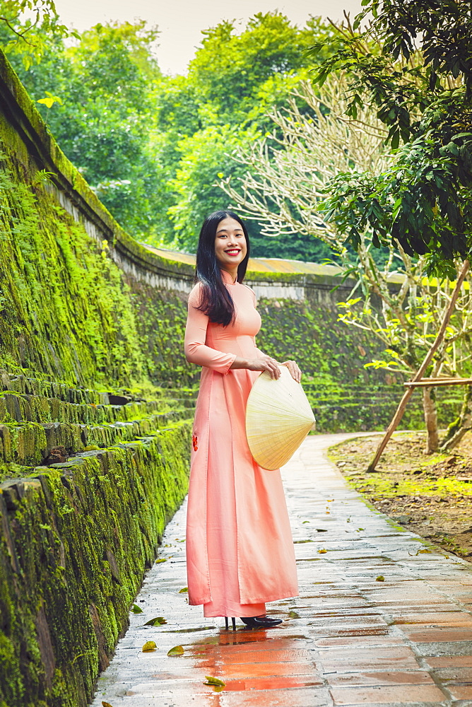 A young Vietnamese woman in an Ao Dai dress and conical hat at a Buddhist temple, Hue, Vietnam, Indochina, Southeast Asia, Asia