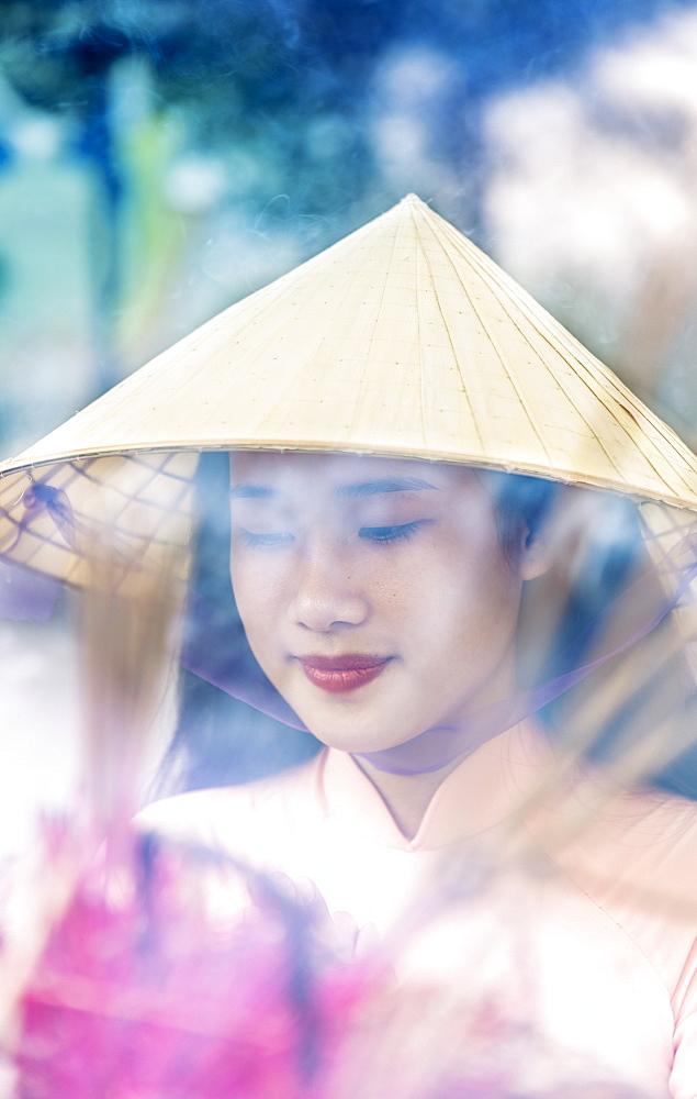 A young Vietnamese woman in a conical hat making incense offerings at a Buddhist temple, Hue, Vietnam, Indochina, Southeast Asia, Asia