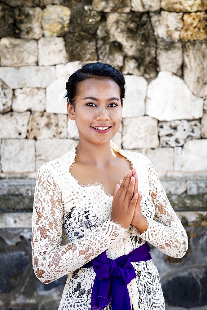 A young Balinese woman in a local temple dress making a formal greeting and smiling, Bali, Indonesia, Southeast Asia, Asia