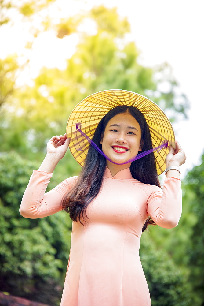 A young Vietnamese woman in a traditional Ao Dai dress and conical hat and smiling, Hue, Vietnam, Indochina, Southeast Asia, Asia