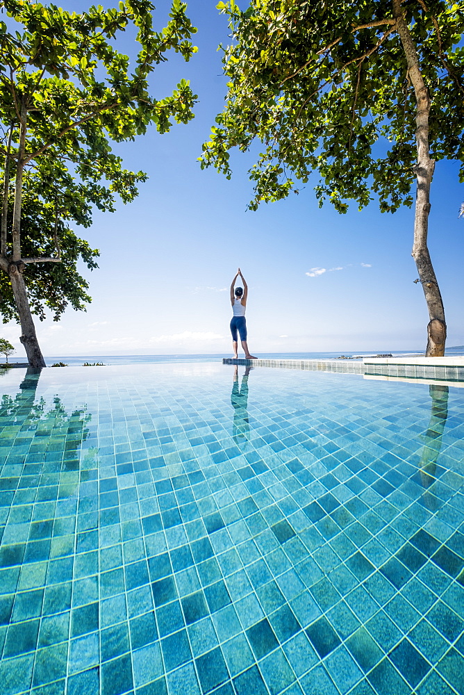 An Asian woman doing yoga exercises on the edge of an infinity swimming pool next to the sea, Indonesia, Southeast Asia, Asia