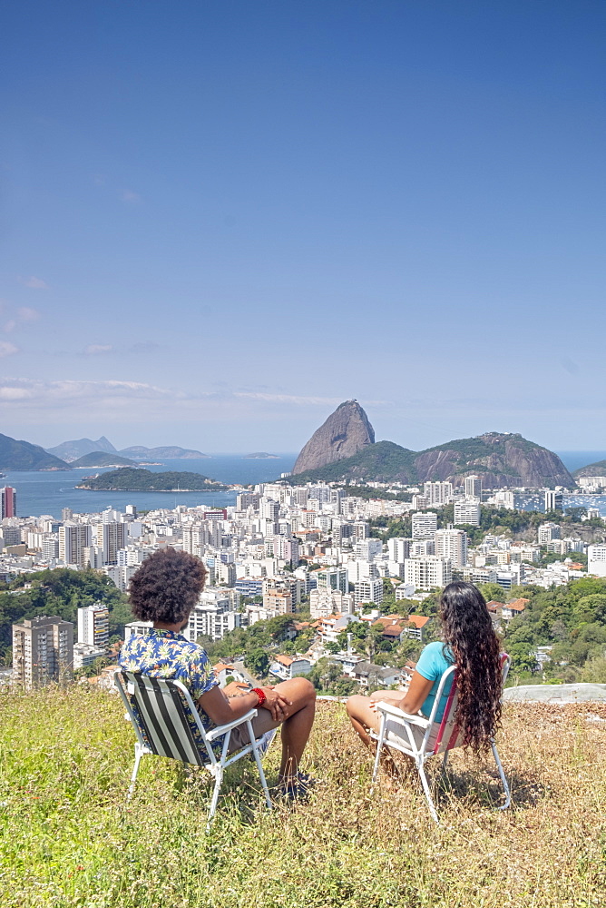 A multi-ethnic couple sitting together and looking out over Sugar Loaf mountain and the Rio skyline, Rio de Janeiro, Brazil, South America