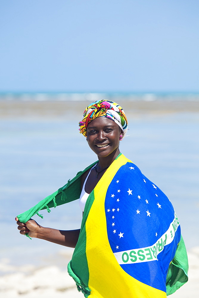 A young black Brazilian woman wearing a head scarf and a wrap showing the national flag, smiling and looking to camera, Brazil, South America