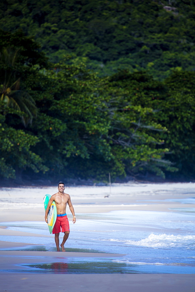 Brazilian male surfer with a Brazilian flag surfboard on a beach in Rio de Janeiro state, Brazil, South America