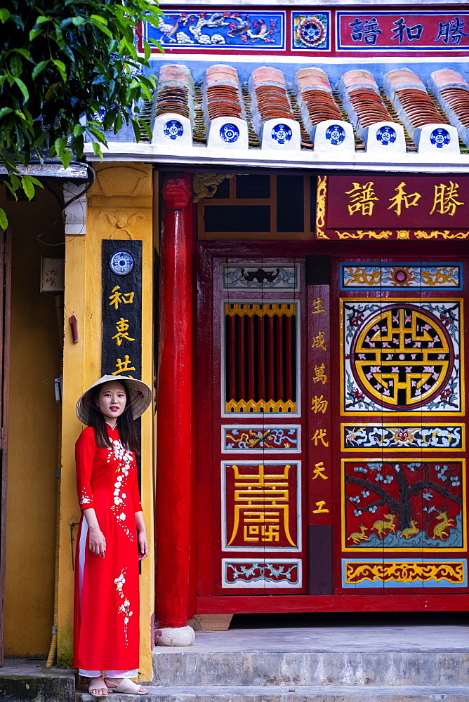 A young Vietnamese woman wearing a traditional Ao Dai dress and standing outside a temple in the historic town centre, Hoi An, Vietnam, Indochina, Southeast Asia, Asia