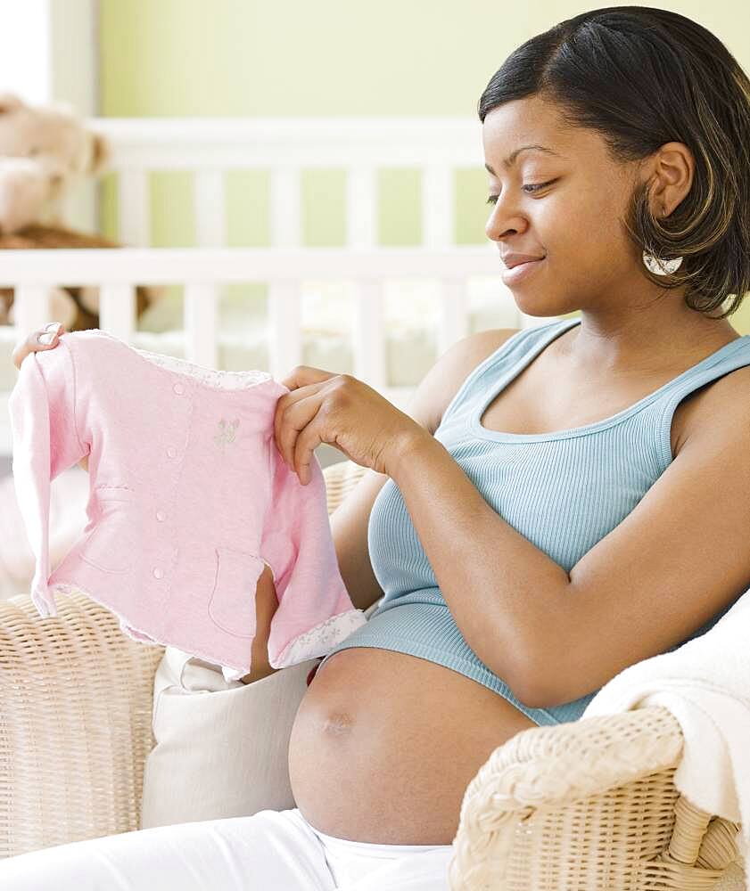 Pregnant African American woman holding baby clothes