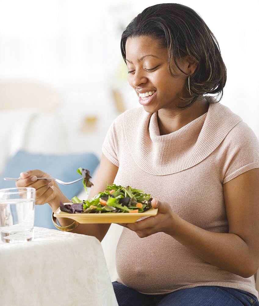 Pregnant African American woman eating salad