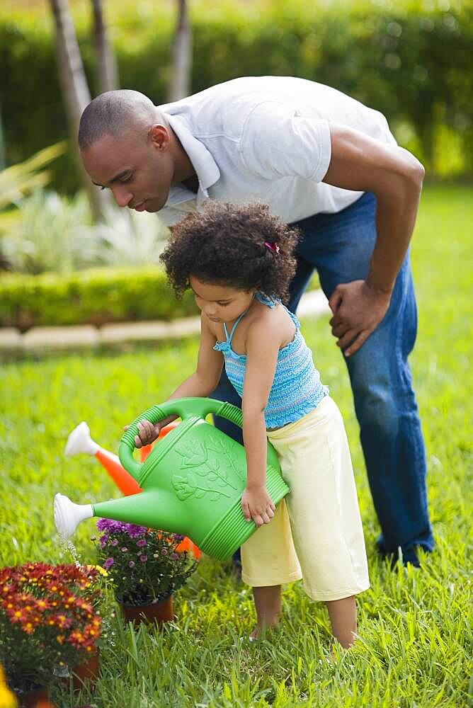 African father and daughter watering flowers