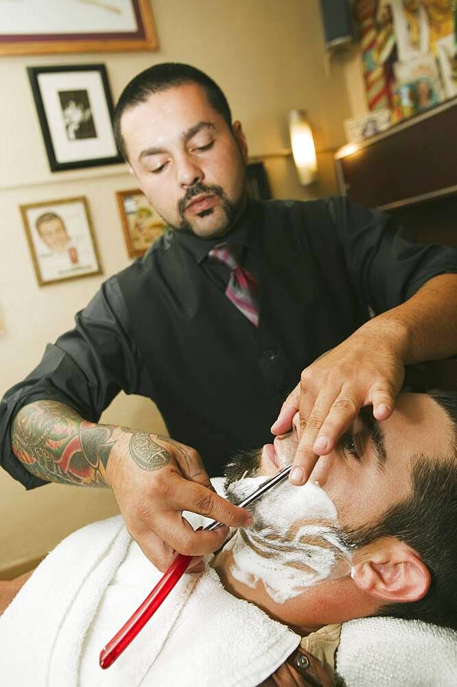 Hispanic barber shaving man's face