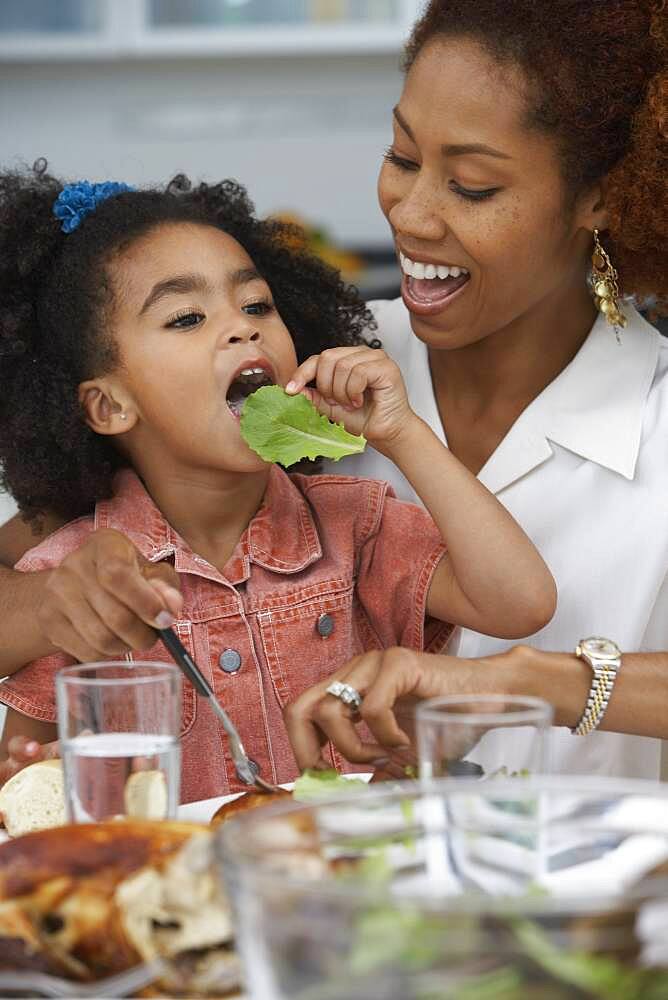 Young girl eating a leaf of lettuce at the dinner table