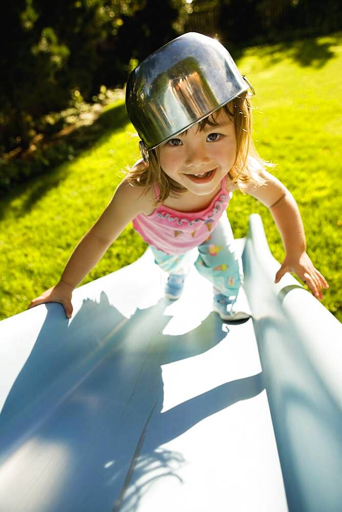 Portrait of girl climbing slide with bowl on head