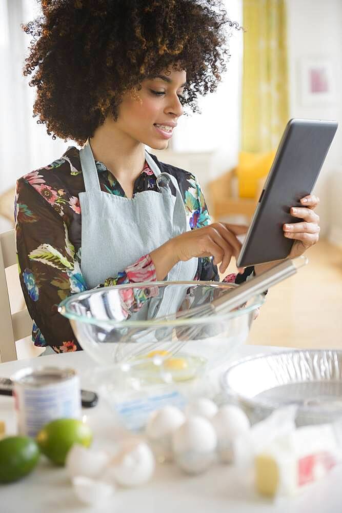 Mixed race woman baking with recipe on digital tablet