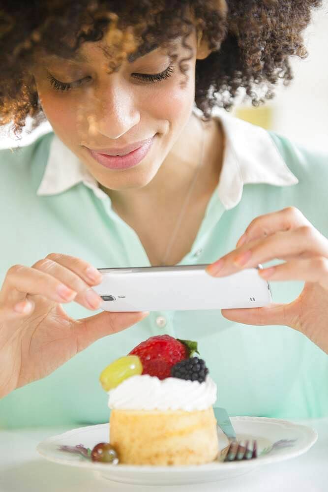 Mixed race woman taking cell phone photograph of dessert