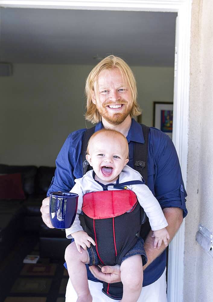 Caucasian father wearing son in harness in doorway