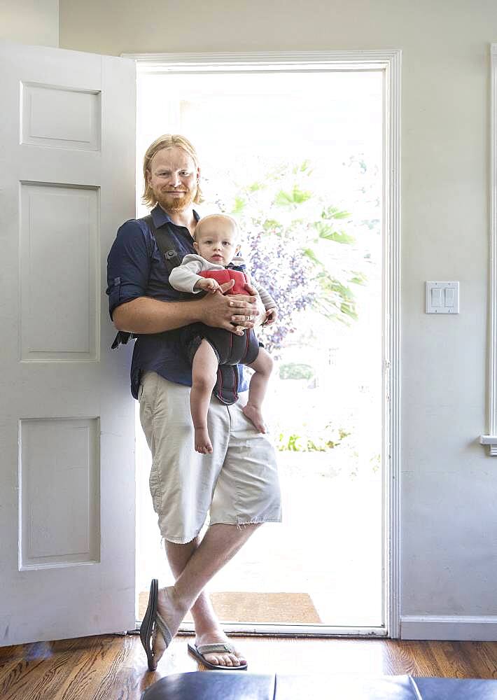 Caucasian father wearing son in harness in doorway