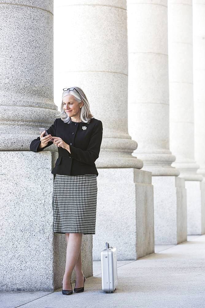 Caucasian businesswoman using cell phone under columns