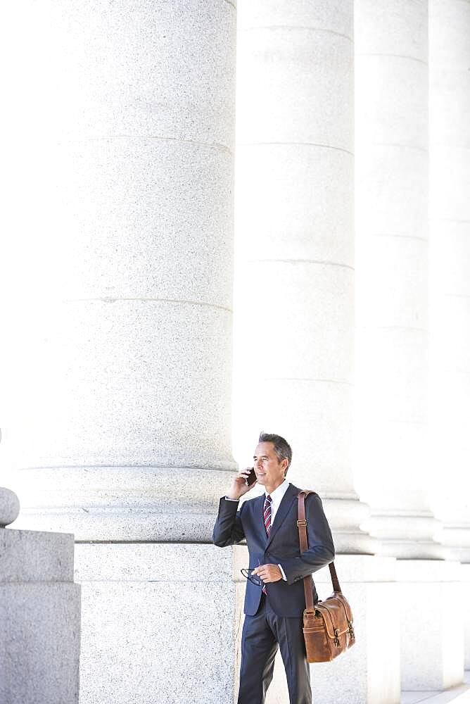 Mixed race businessman talking on cell phone under columns