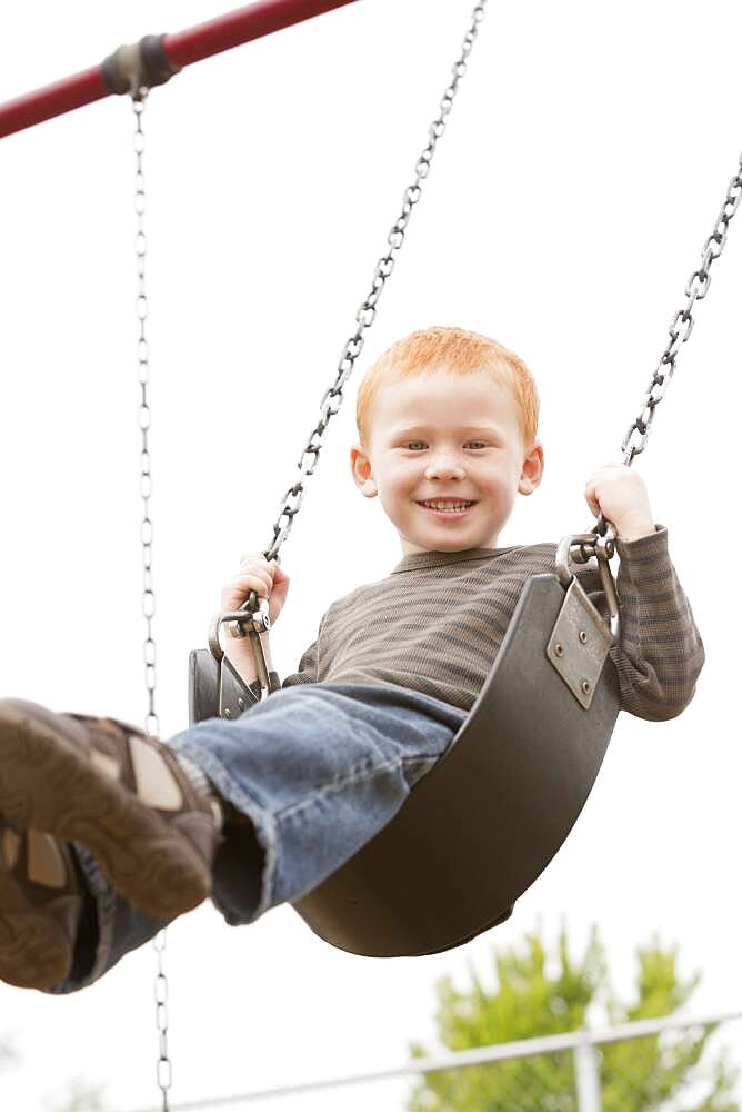 Caucasian boy sitting on playground swing