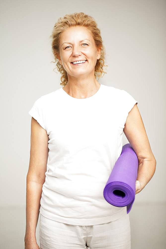 Smiling woman holding exercise mat