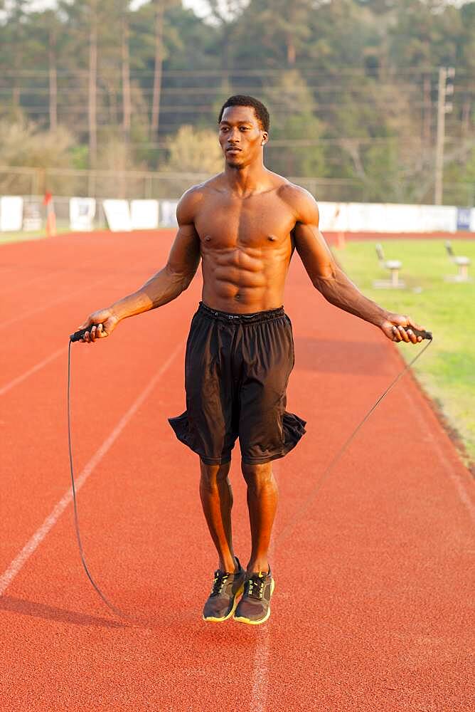 Black athlete jumping rope on track in sports field