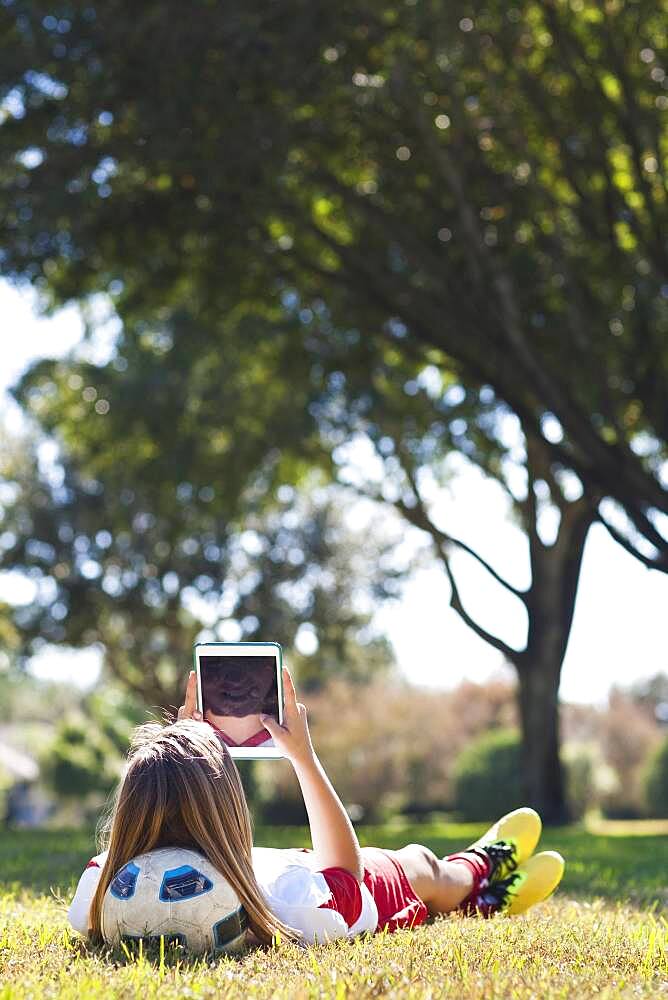 Caucasian soccer player laying in grass using digital tablet