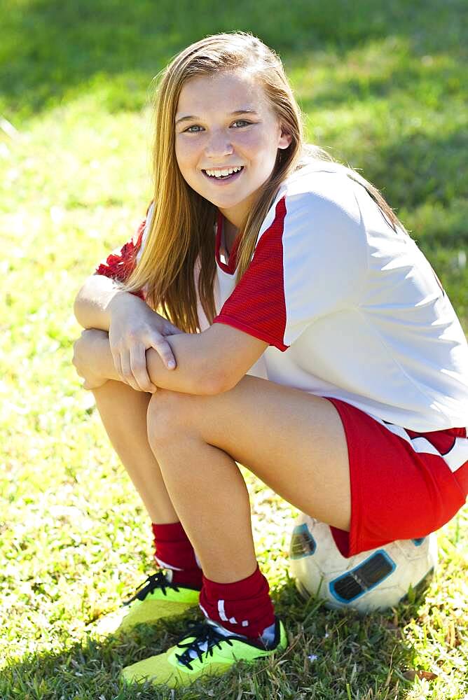 Caucasian soccer player sitting on ball in grass,