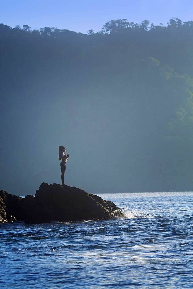 Mixed race woman standing on rock over ocean