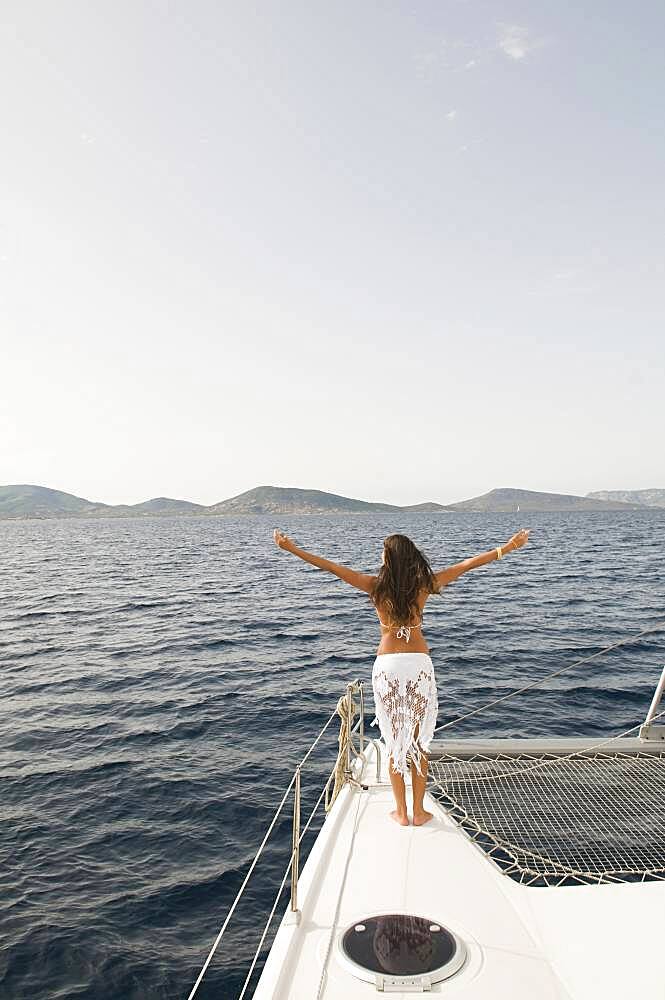 Woman standing with arms outstretched on sailboat deck